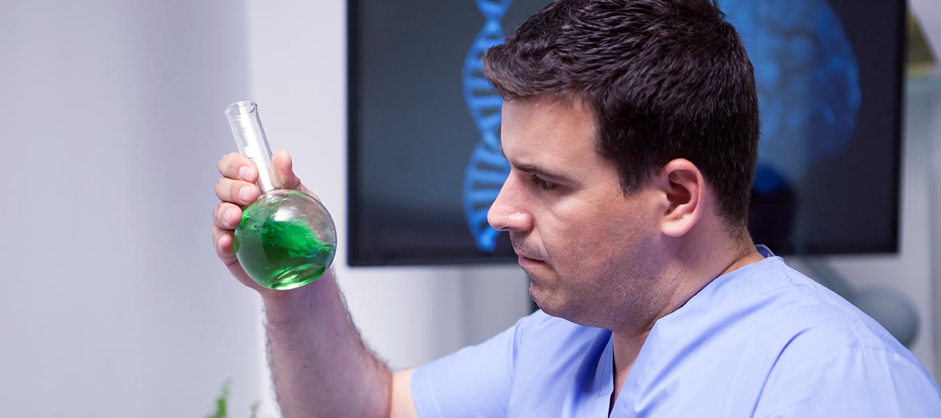 Man in medical attire looking at a beaker with green liquid, probably cannabis extract.