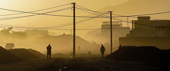 Dusty environment, with silhouette of men walking around against a mountainous background.