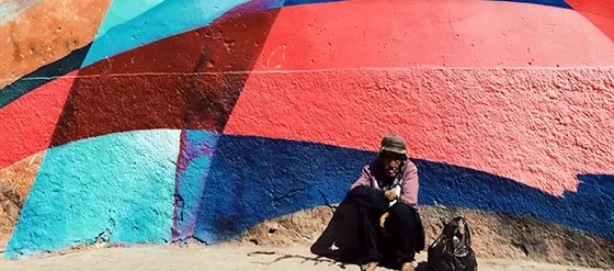 Man in hat sitting crouched against a colorful building
