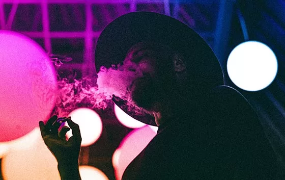 Man in hat smoking a joint with colorful lighting.