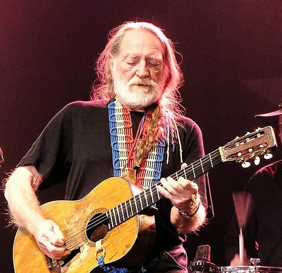 Willie Nelson on stage, playing an acoustic guitar